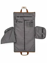 Bolso de viaje color beige con detalles en marrón, cuenta con dos bolsillos frontales, uno con solapa y otro con cierre, y manijas superiores reforzadas.