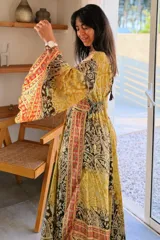 Vestido largo de estilo bohemio, color azul con estampado floral en tonos blancos y detalles geométricos en el escote y la cintura. Posee escote en V con cordones ajustables, mangas amplias tipo kimono y una silueta fluida y holgada.