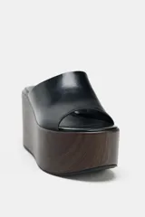 Sandalia tipo mule de plataforma alta, color negro, con tira ancha delantera de cuero y suela plataforma gruesa con acabado de madera oscura.