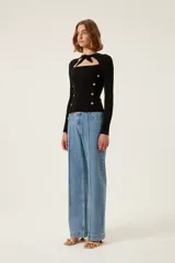 Suéter de punto negro con cuello anudado y abertura sobre el pecho. Presenta detalle de botones a presión con forma de sol en la parte delantera y bordado "TRS".