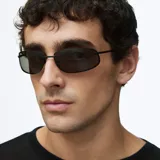 Lentes de sol con montura metálica negra y lentes rectangulares de cantos redondeados. Presentan un diseño envolvente inspirado en los años 2000 con patillas de acetato.