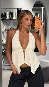 Top halter de tejido de punto color blanco, con escote en V pronunciado, diseño abierto en el frente y bajo asimétrico en punta.