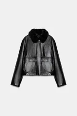 Chaqueta de efecto piel en color negro, con cuello de solapa con aplicación de pelo sintético, manga larga y bolsillos frontales de plastrón con solapa. Cierre frontal con cremallera y botones ocultos bajo solapa.