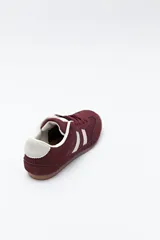 Zapatilla urbana de perfil bajo con diseño retro, confeccionada en poliuretano con detalles en textura tipo gamuza. Presenta puntera redondeada, cordones clásicos y suela de goma color caramelo.