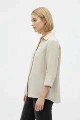 Camisa de algodón color beige, de corte holgado, con mangas tres cuartos, cuello camisero y cierre frontal de botones.