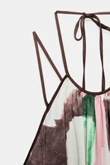 Vestido largo de tela fluida con estampado abstracto en tonos rosado, verde y marrón sobre fondo blanco. Presenta cuello halter con tiras ajustables anudadas en la nuca y tirantes finos que se cruzan en la espalda.