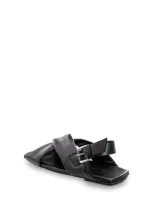 Sandalias bajas color blanco hueso, con punta cuadrada, tiras anchas cruzadas en el empeine y ajuste con hebilla en el tobillo.