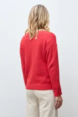 Cardigan de punto color rojo con cierre frontal de botones y bordados de flores en diversos colores. Presenta cuello redondo y mangas largas con puños acanalados.