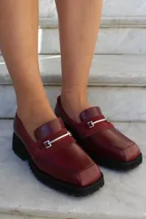 Mocasín de cuero vacuno color marrón, con suela track de goma negra, puntera cuadrada y detalle de herraje metálico sobre una banda de gamuza en el empeine.