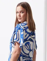 Blusa de seda fría con estampado abstracto en blanco y azul. Tiene cuello redondo con frunce, escote en V con botón y mangas cortas amplias.