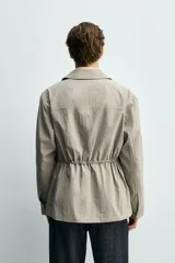 Parka relaxed fit color gris, confeccionada en tejido técnico ligero, con cuello solapa, manga larga con puño abotonado, cuatro bolsillos de plastrón con solapa en el frente, cintura ajustable con cordón y cierre frontal de botones.