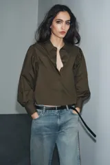 Camisa de popelín color verde militar, con cuello solapa, mangas largas abullonadas terminadas en puño, bajo recto y cierre frontal con botones ocultos por solapa.