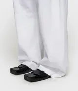 Pantalón de algodón orgánico blanco, de corte ancho y relajado, con cintura elástica en la parte trasera, cierre de botón y cremallera, y bajo sin rematar.