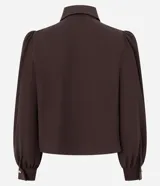 Camisa de crepé color blanco, con cuello inglés, manga larga abullonada con puños abotonados y cierre frontal oculto con botón diferenciado en el cuello.