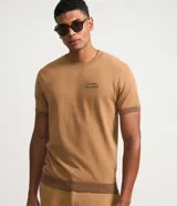Remera de punto color tostado con cuello redondo, mangas cortas y detalle de bordado con la frase "Savane tropicale" en el pecho.
