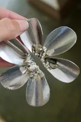 Par de caravanas plateadas con forma de flor, con pétalos metálicos y centro decorado con cuentas y piedras brillantes.