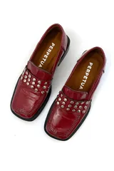 Mocasín de cuero color cereza con apliques metálicos plateados en la parte delantera, suela plana y taco cuadrado bajo color negro.