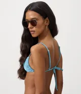 Top de bikini bandeau celeste con acabado satinado, breteles finos y un llamativo aplique metálico dorado en el centro.