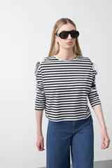 Remera de manga larga a rayas horizontales blancas y negras, con escote redondo y aberturas en los hombros sujetas con lazos regulables de tela a rayas.