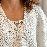 Ruana tejida de lana color blanco crudo, con diseño amplio y envolvente, escote en V y detalles de encaje bordado a mano en los hombros.