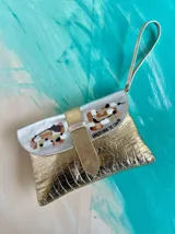 Sobre de mano Carolina De Cunto modelo Saria, confeccionado en cuero dorado brillante con textura y solapa plateada con detalles pintados a mano. Cuenta con tira de muñeca y cierre con broche imán.
