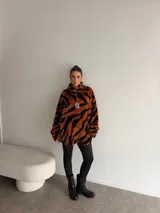 Buzo de peluche con estampado animal print, cuello alto con cierre frontal parcial y detalle de etiqueta decorativa en el pecho.