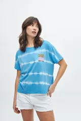 Remera de manga corta con teñido artesanal tipo batik en tonos de azul y blanco, con un pequeño estampado gráfico en el pecho.