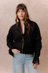 Chaqueta de gamuza sintética color negro, de calce relajado y largo a la cintura. Presenta cuello mao con cierre a presión, cierre frontal metálico, bolsillos delanteros de placa y puños con broche regulable.