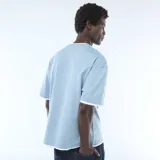 Remera celeste de manga corta con diseño de doble capa efecto 2 en 1, con detalles en color blanco visibles en el cuello, mangas y ruedo.
