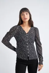 Blusa rosa con estampado de flores blancas y amarillas, cuello en V, manga larga abullonada y cierre frontal con botones.