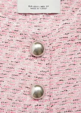 Chaqueta de tweed en tonos rosados, con cuello redondo, manga larga y cierre frontal con botones metálicos. Presenta dos bolsillos de parche en la parte delantera y diseño entallado con forro interior.