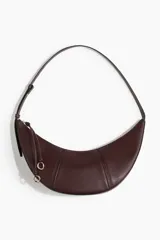 Cartera marrón de diseño curvo con costuras visibles, correa ajustable, cierre superior y tiradores largos con detalle de nudo y argollas doradas.