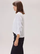 Remera de algodón color blanco, con cuello redondo y mangas tres cuartos con volados escalonados y detalles de pespuntes.