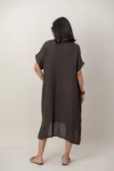 Vestido midi de lino color beige, de corte holgado y silueta acampanada. Cuenta con cuello redondo, mangas cortas amplias, bolsillos laterales y detalles de recortes horizontales en la falda con terminación asimétrica más larga en la parte trasera.