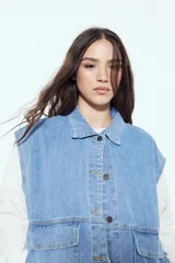 Chaleco de jean con corte oversized, diseño sin mangas, cuello camisero, cierre frontal con botones metálicos y bolsillos frontales tipo cargo.