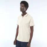 Remera polo de piqué de algodón color beige claro, de manga corta, con cuello y bordes de mangas en ribete negro y blanco.