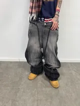 Jean de corte amplio en color negro con efecto acid wash. Presenta cierres laterales metálicos que permiten ajustar la silueta entre corte recto, oxford o baggy. Incluye una estampa gráfica de gran tamaño en la parte trasera con detalles bordados, bolsillos amplios y una etiqueta de cuero legítimo en la cintura.