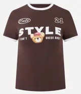 Remera de corte ajustado color marrón chocolate, con cuello redondo y bordes de mangas en color blanco. Presenta un estampado frontal con la palabra 'STYLE' en letras grandes, un oso pequeño con gorra y el texto 'Cute' y '21'.