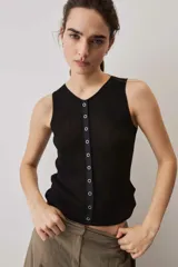 Blusa musculosa de punto color negro, con textura acanalada y silueta ajustada al cuerpo, decorada con una línea de ojalillos metálicos frontales.