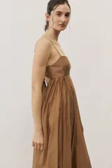Vestido largo color beige con escote recto, tirantes finos y falda amplia con diseño drapeado.
