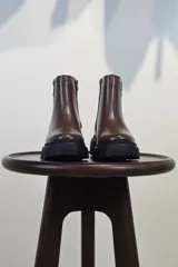 Bota de caña corta color marrón, con cierre lateral y suela track negra de goma con plataforma.