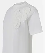 Remera blanca de algodón con cuello redondo y corte boxy, con apliques de flores de tejido en relieve en la zona del pecho.