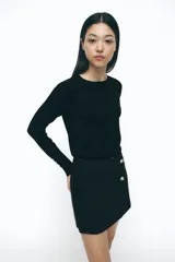 Falda pantalón negra de tiro alto con diseño cruzado frontal, dos botones dorados decorativos y falsos bolsillos de doble vivo.