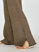Pantalon de corte recto y pierna ancha, confeccionado en lino color beige. Presenta un diseño de tiro medio con aberturas laterales en el ruedo y detalle de bordes desflecados.