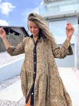 Vestido camisero de corte holgado y diseño escalonado, con estampado animal print en tonos beige y negro. Presenta cuello camisero, cierre frontal con botones y mangas largas con puños.