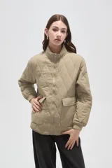 Campera acolchada de poliamida en color beige, con diseño de costuras en rombos, cuello alto, cierre frontal y bolsillos delanteros con solapa.