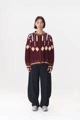 Campera tipo bomber tejida con diseño jacquard geométrico en tonos azul marino, blanco, rojo y verde. Presenta cierre frontal completo, cuello, puños y ruedo acanalados en color verde y blanco, con corte oversized y hombros caídos.