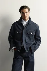 Campera de denim azul oscuro de corte cropped, con cuello camisero, bolsillos delanteros con solapa y cierre frontal oculto con botones metálicos.