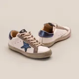 Zapatillas bajas de cuero vacuno color blanco, con estrella azul metalizada en el lateral, detalles en gamuza color aluminio y contrafuerte azul metalizado.