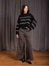 Buzo corto de tejido de punto en color negro, con diseño de textura en relieve y líneas horizontales blancas. Presenta cuello redondo y mangas largas con puños ajustados.